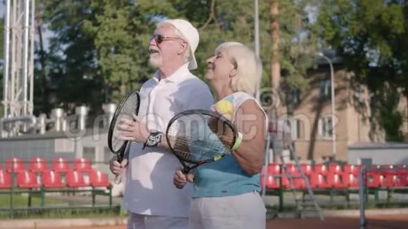 可爱的微笑成熟的夫妇准备在网球场上打网球户外休闲活动高级官员视频的预览图