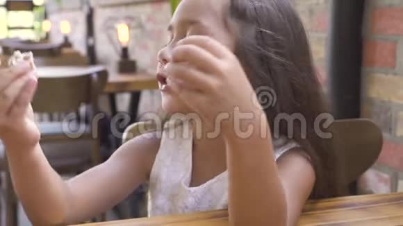 肖像小女孩吃甜蛋糕在咖啡馆的桌子上微笑面对可爱的女孩微笑着吃着甜馅饼视频的预览图