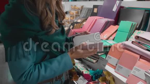 美丽的白种人女孩穿着蓝色夹克和绿色围巾在商店里挑选和购买办公用品和笔记本视频的预览图