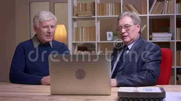 老商人坐在桌子旁拿着笔记本电脑认真讨论这个项目的画像视频的预览图