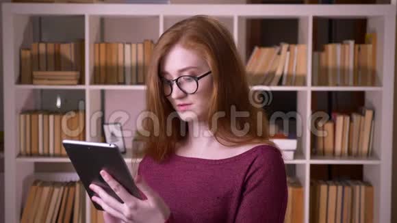 在大学里戴着眼镜在平板电脑上浏览的年轻红发美女白人女学生视频的预览图