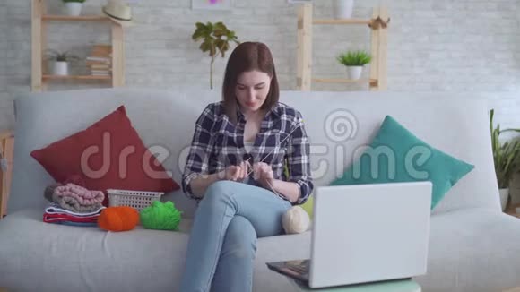 坐在笔记本电脑前沙发上学习编织的女人视频的预览图