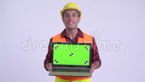 年轻快乐的西班牙裔建筑工人一边说一边展示笔记本电脑视频的预览图