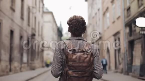 带着棕色背包和戴着带支票夹克的耳机的年轻游客的后景视频的预览图