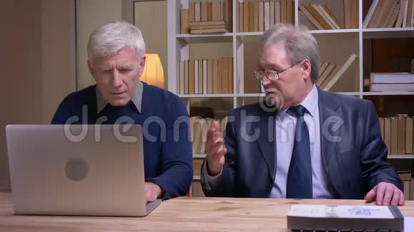 老商人坐在桌旁拿着笔记本电脑积极讨论合同的画像视频的预览图