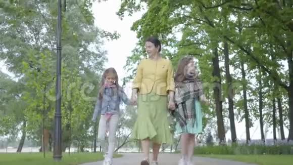 成熟优雅的女人和她的两个孙女在公园里散步幸福的家庭牵着手祖母花钱视频的预览图