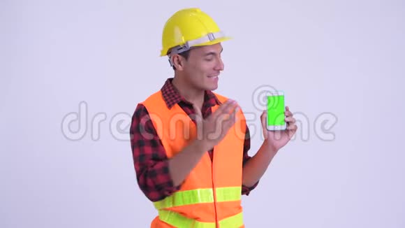 年轻快乐的西班牙裔建筑工人一边打电话一边说话视频的预览图