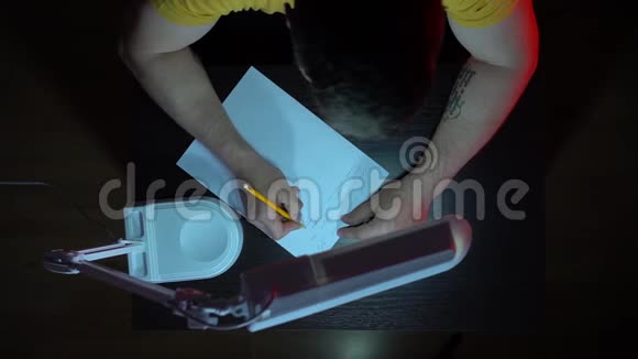 从上面看一个穿黄色T恤的人在黑暗中的桌子上工作一个人用手在纸上写字视频的预览图