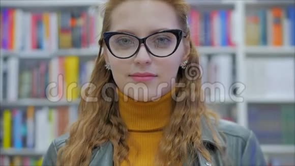 特写镜头幸福漂亮的年轻女子戴眼镜的女孩学生微笑着看着站在图书馆里的镜头视频的预览图