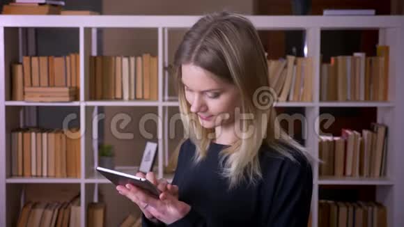 一位年轻迷人的女学生用平板电脑看着镜头在室内开心地微笑着的特写镜头视频的预览图