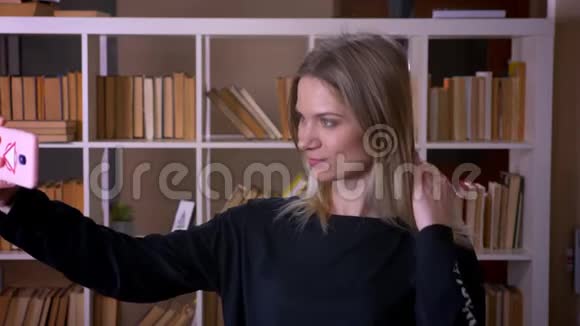 在大学图书馆里一位年轻迷人的女学生在室内打电话自拍的特写镜头视频的预览图