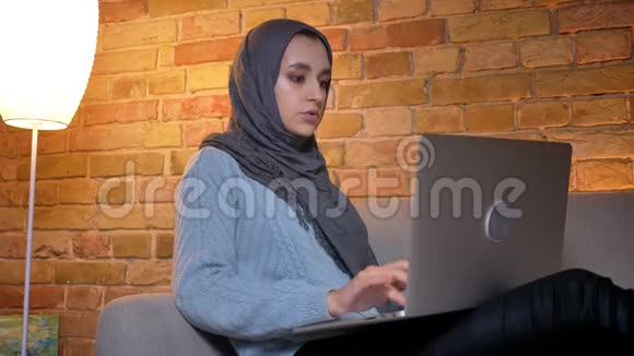 年轻有魅力的穆斯林女学生戴着头巾坐在电脑前上网学习的特写镜头视频的预览图
