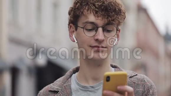 戴眼镜戴耳机使用智能手机打字信息在社交场合使用夹克的千禧嬉皮士视频的预览图