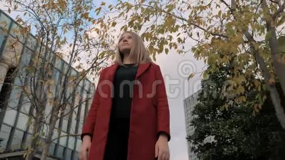 穿着红色外套的年轻女子站在秋天五彩缤纷的公园里欣赏秋天的树叶视频的预览图