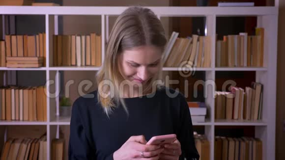 在大学图书馆室内用手机发短信的年轻有魅力女学生特写镜头视频的预览图