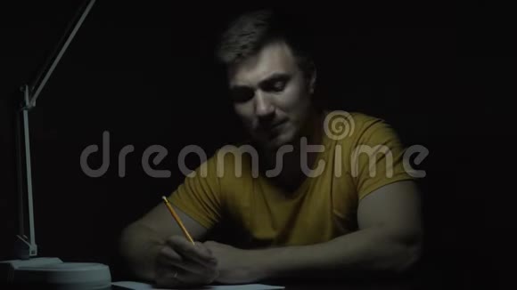 一个穿黄色T恤的人在黑暗中的桌子上工作一个人用铅笔在纸上用手写字视频的预览图
