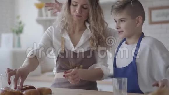 漂亮的快乐女人和她的四个十几岁的儿子站在桌子旁吃着派穿围裙的男孩拥抱视频的预览图