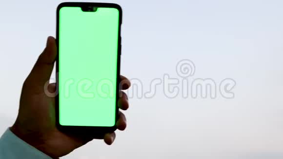 男人拿着一部绿色屏幕的智能手机对着天空视频的预览图