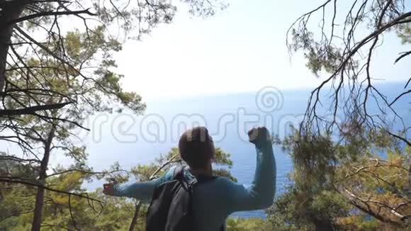 快乐的徒步旅行者带着背包在山的边缘欢呼胜利地举起双手男性游客视频的预览图