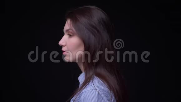 年轻的黑发女商人穿着蓝色衬衫的肖像变成了在黑色背景下认真观看的镜头视频的预览图