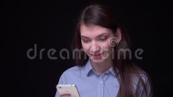 年轻的黑发女商人穿着蓝色上衣微笑着谦虚地看着黑色智能手机的画像视频的预览图