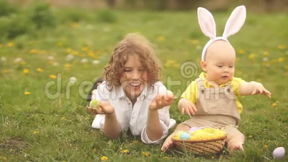 一岁的孩子穿着兔子服装哥哥坐在公园里玩复活节彩蛋视频的预览图