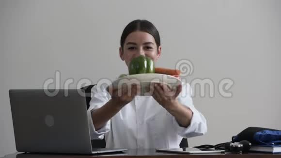 一位专业的年轻女医生坐在办公室里提供蔬菜作为维生素和健康食品视频的预览图