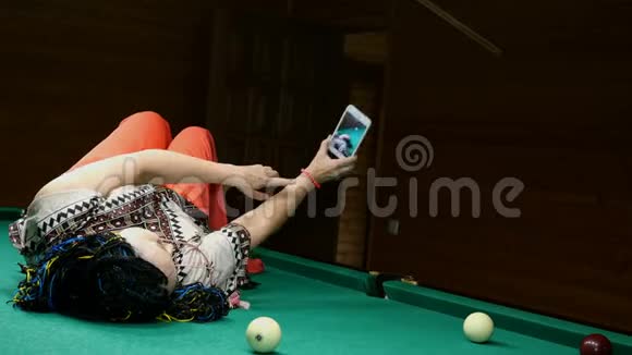高级女性在智能手机上自拍躺在台球室的台球桌上视频的预览图