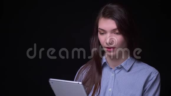 年轻的黑发女商人穿着蓝色衬衫微笑着看着黑色背景的平板电脑视频的预览图