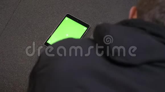 成年肌肉运动员用绿色屏幕推着平板电脑的特写镜头躺在室内视频的预览图