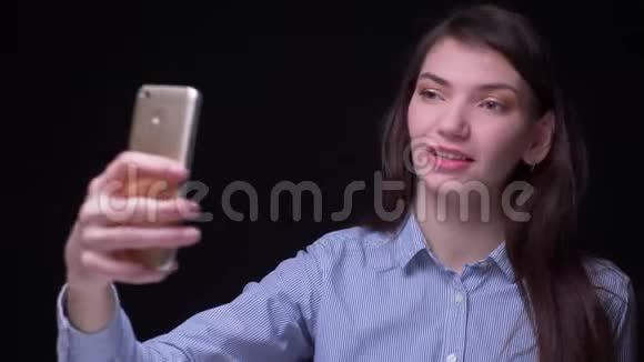 漂亮的黑发女商人穿着蓝色衬衫用智能手机制作自拍照片在黑色背景下快乐视频的预览图