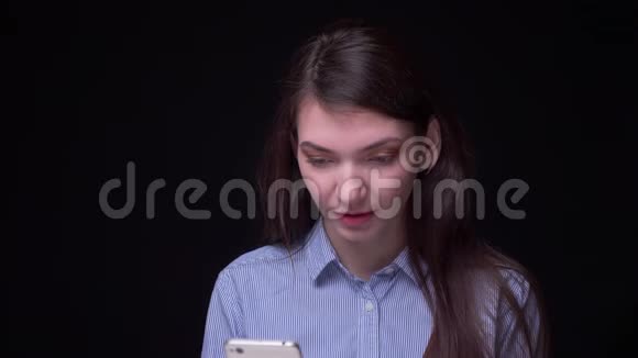 漂亮的黑发女商人穿着蓝色衬衫在智能手机上快乐地工作转向相机对着黑色微笑视频的预览图