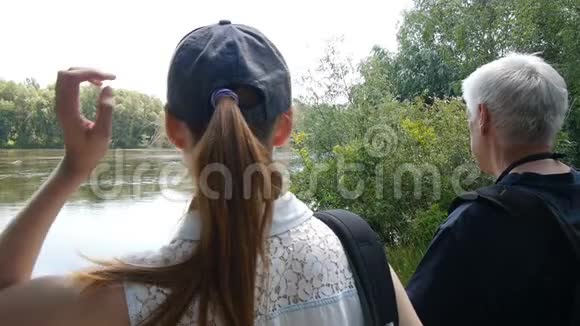 男人和女孩一起远足带背包的徒步旅行者他们停在河岸上看着它令人感动的女孩视频的预览图