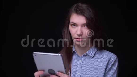 年轻的黑发女商人穿着蓝色衬衫用平板电脑工作的肖像转向相机严肃地看着视频的预览图