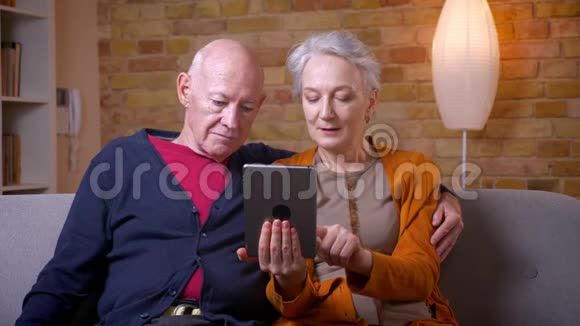 高级白种人配偶一起使用平板电脑坐在客厅的沙发上视频的预览图