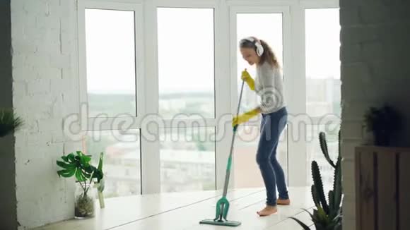 美丽的年轻女子正在清洁灯光的现代化工作室有全景的窗户女孩正在洗地板玩得很开心视频的预览图
