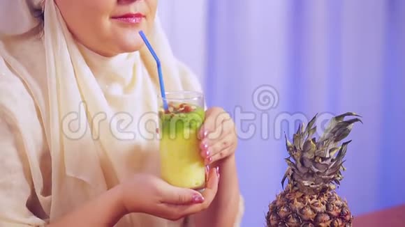 一位年轻的穆斯林妇女戴着一条浅色围巾手里拿着一个杯子手里拿着一块水果冰沙拿着一根东西视频的预览图
