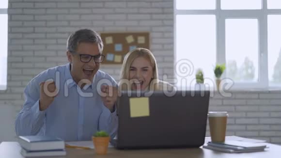 快乐的商人兴奋地看着坐在工作场所的笔记本电脑屏幕庆祝商业成功在获胜视频的预览图
