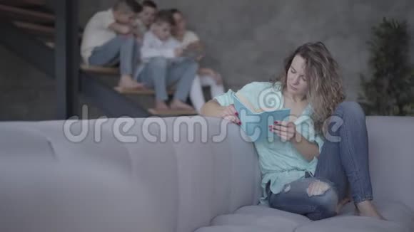 美丽的母亲坐在沙发上给儿子们读一本书四个可爱的弟弟坐在视频的预览图