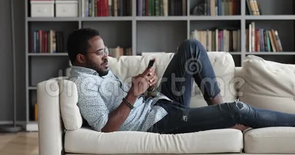 非洲年轻人在家里沙发上打电话放松视频的预览图