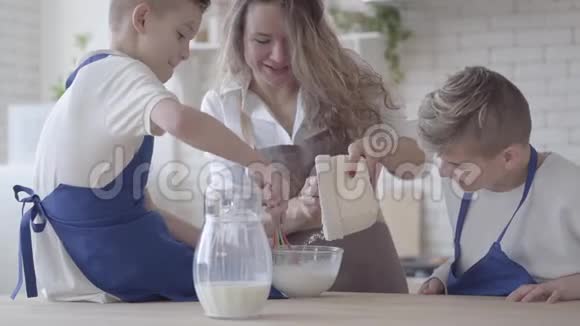 肖像漂亮的女人和她的两个儿子在厨房里做饭做面团男孩们帮助母亲做食物妈妈视频的预览图
