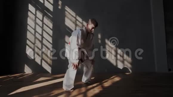 男勇敢运动员正在准备跆拳道比赛穿着白色和服光着脚阳光从窗户射进来视频的预览图