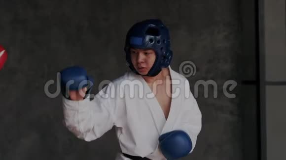 年轻的巧手在混合武术中攻击他的对手带手套和和和服的带防护头盔的男孩教室视频的预览图