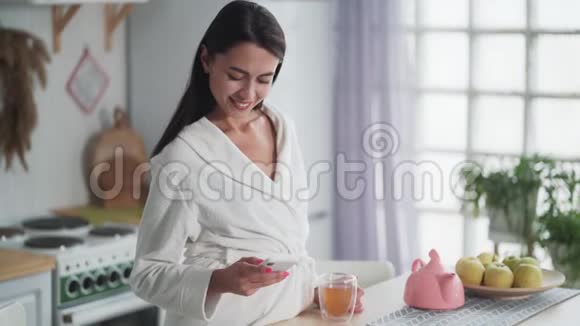 穿着白色浴袍的女人在手机上发信息用手机在家工作视频的预览图