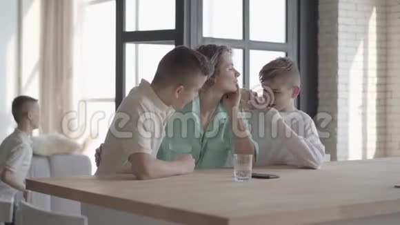年轻漂亮的女人一头卷发站在家里的柜台前她的十几岁的小儿子们一起玩耍视频的预览图