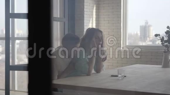 儿子拥抱着一个疲惫的母亲站在室内的桌子旁兄弟情谊家庭关系视频的预览图