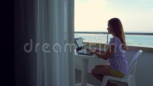 这个女孩在酒店阳台上的笔记本电脑上工作视频的预览图