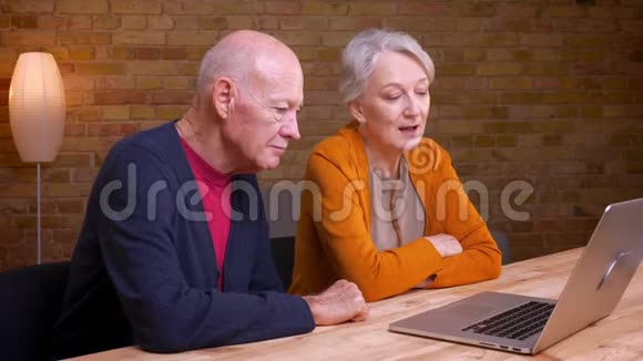 两位白发苍苍的老白种人夫妇在笔记本电脑上用视频聊天在办公室里很开心视频的预览图