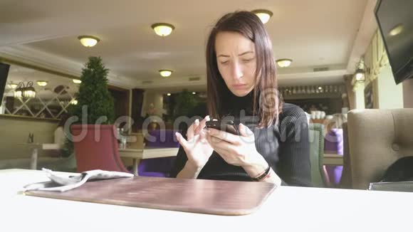 年轻的馄饨在工作休息的时候坐在舒适的咖啡店里一边用手机一边迷人的快乐女性阅读视频的预览图