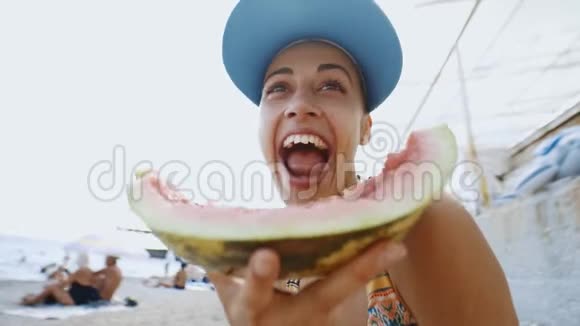 在海滩上吃一大块西瓜的滑稽少女的广角镜头视频的预览图